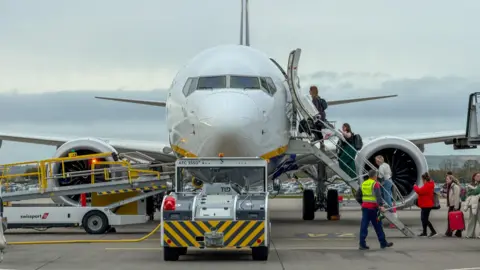 A plane on the runway at Bristol Airport. People are boarding it via the steps. 