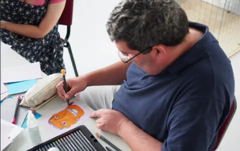 Suffolk Art Link  Man in a navy top using a felt tip pen to colour a portrait