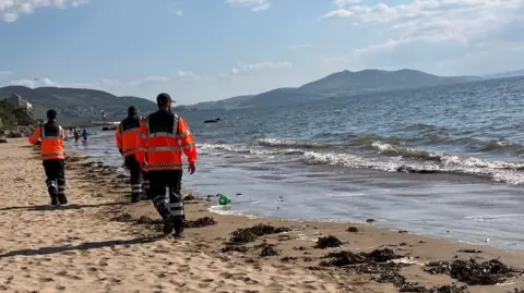 Three people in high viz walking along a shoreline.