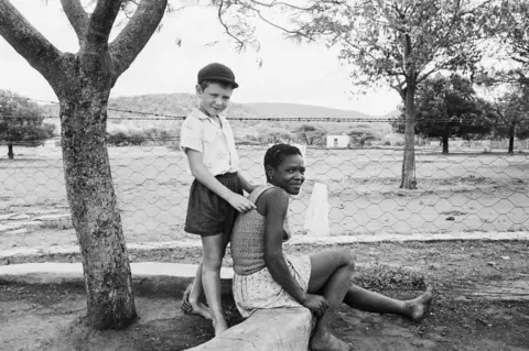 Photograph by David Goldblatt  A farmer's son with his nursemaid, Heimweeberg, Nietverdiend, Western Transvaal. 1964.