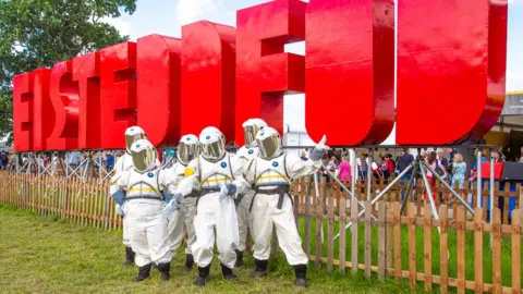 NAtional Eisteddfod Eisteddfod sign with individuals dressed as astronauts in front of the sign