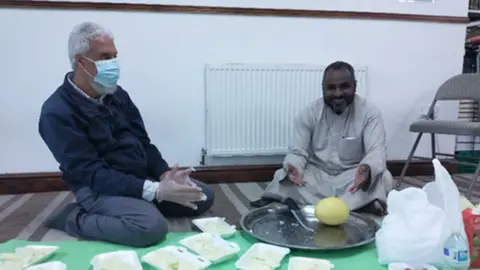 Two men kneeling with food.