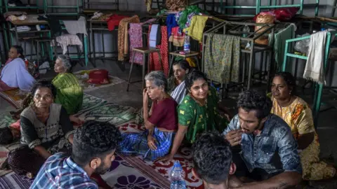 Getty Images Women and men sitting in a refugee shelter