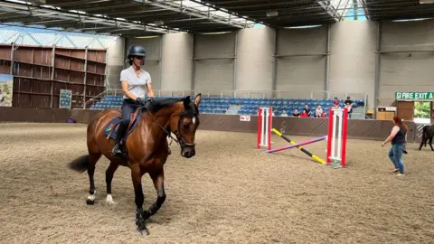 Mia Benton Woman riding a horse at an indoor arena