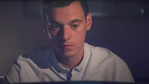 A man with brown hair and wearing a light blue shirt looks in contemplation.
