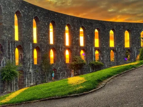 Aileen Gillies A large stone structure with the sun shining through the window frames