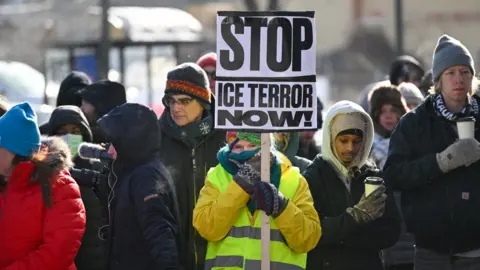 A woman holds a sign reading 'Stop ICE terror now!' at a makeshift memorial for Alex Pretti in south Minneapolis