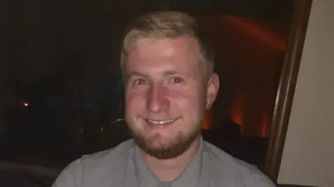Jack Bristow is smiling broadly at the camera. He has fair hair and a beard and wears a grey shirt.