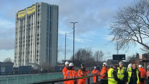 The 15-storey grey concrete building before it was demolished. It had been mainly hollowed out. A large, yellow "Thompsons" sign was draped at the top.