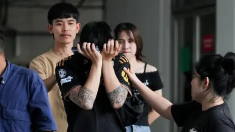A person with their head in their hands as family members and relatives mourn as they receive the body of a victim at the Police Hospital morgue