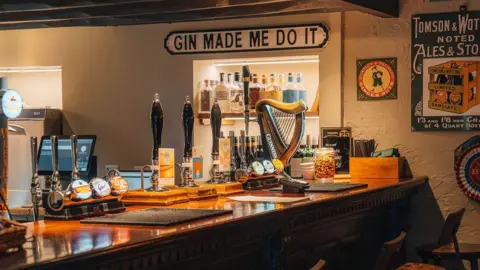 The Bryntirion Inn A man wearing a white shirt pulling a pint on lager. There are glasses on shelves behind him