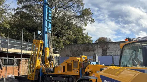 Delapre Abbey Yellow construction machinery sits dormant next to brick walls with metal scaffolding. 