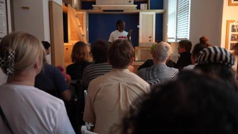 Performer Lisa Ogun tells an audience about a donor's walking stick