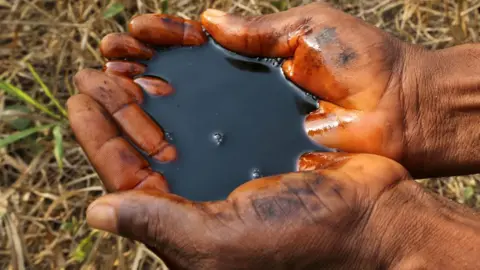 A man holds a pool of black oil in the palm of their hands in Ogoniland, Nigeria