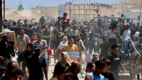 Dozens of Palestinians walking at an aid distribution centre in Gaza. Some are carrying supplies.