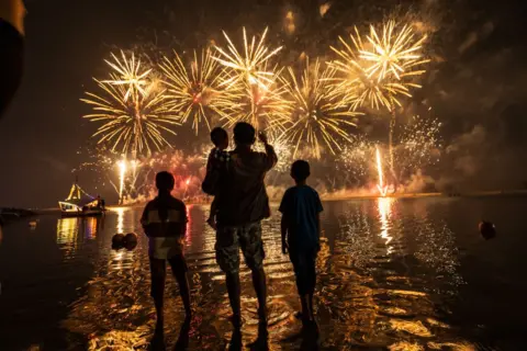 YASUYOSHI CHIBA/AFP Penduduk setempat menonton kembang api di kota Jakarta, saat mereka merayakan tahun baru di dekat Pantai Ancol di Indonesia, pada 1 Januari 2025.