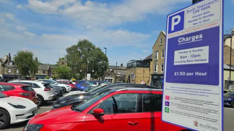 Aisha Iqbal/BBC A car park full of cars, and a close up of a sign indicating charges apply from 8am to 10pm every day at a flat rate of £1.50 an hour.