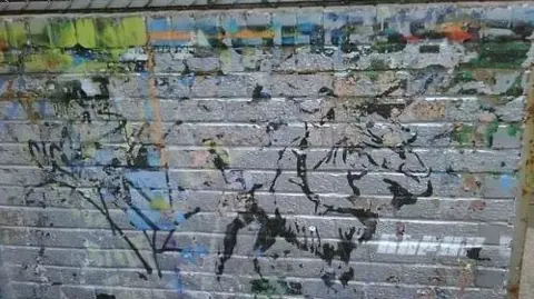 Faint graffiti on a silver wall, with the word "Banksy" top right