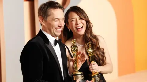 Sean Baker and Samantha Quan smile with Oscars