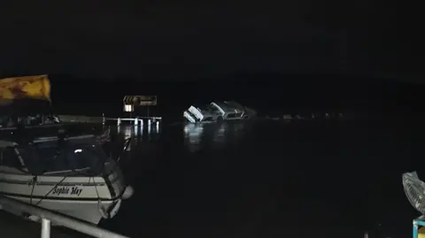 Nottinghamshire Fire and Rescue Service A boat is listing towards the side in a marina at night, in the foreground another boat can be seen to the left