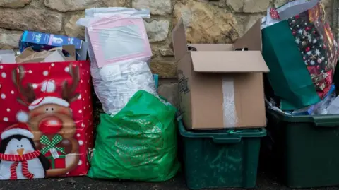 Rubbish left out for bin collections - includes brown boxes, a festive large red gift bag and green plastic trays containing more waste