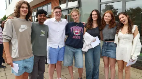 Pates Grammar School Students collecting their A Level results at Pate's Grammar School. Seven students are standing in a line with their arms linked and smiling at the camera, wearing casual clothes