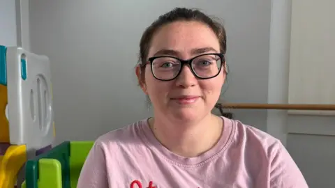 Georgia Hebert is wearing a pink t-shirt that say strawberry. She has brown hair and glasses. 