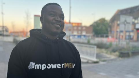 Taicey Gumbeze smiles as he wears a top with the EmpowerMENt logo on the front