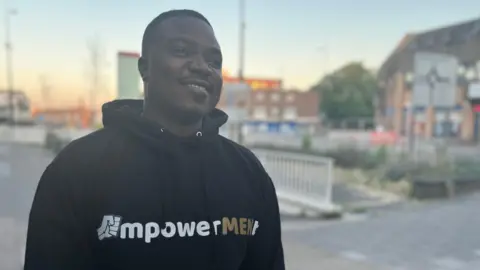 Jon Wright/BBC Taicey Gumbeze smiles as he wears a top with the EmpowerMENt logo on the front