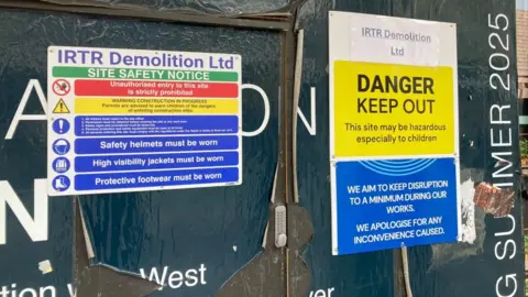 Alex Pope/BBC Signs on a boarded-up door, with a keypad on it, showing that demolition work is due to start. Signs behind it have been ripped. 