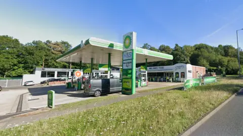 A general view of the BP garage forecourt, with a grey van parked at a pump. There is a blue, clear sky.