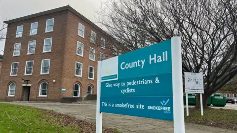 A sign for County Hall in blue and white and a County Hall building behind