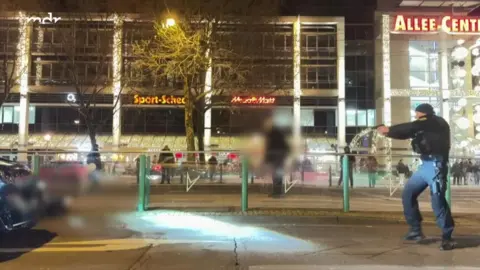 A police office pointing a gun on a street in the dark