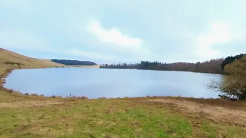 Google A small loch surrounded by woodland on a bright day