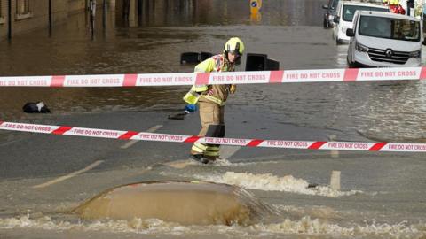 A firefighter stares at water pumping out of the road into a flooded street