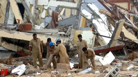 Malacca, India: On January 7, 2005, Indian Air Force personnel attempt to excavate documents from a timekeeping room in Malacca, Kar Nicobar Island, which was completely destroyed by the December 26, 2004 tsunami. Approximately 1,200 people are believed to have died, and 5,600 people are missing in the Andaman Islands. Some 44,000 survivors are being held in shelters on the tropical Indian Ocean archipelago, which is an 800-kilometre (500-mile) stretch of more than 500 islands just east of Sumatra.