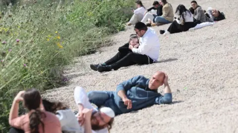 EPA An Israeli father holds his daughter as they and others follow the instructions of the Israeli army Home Front Command to lay on the ground at the side of the road as sirens alert to an incoming missile fired from Iran