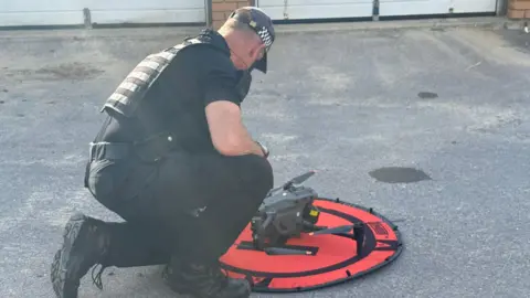 Dorset Police A policeman kneeling near a drone with his back to the camera.