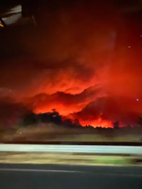 Olivia Jarratt An image taken from the window of a car showing the sky filled with an orange glow from the flames