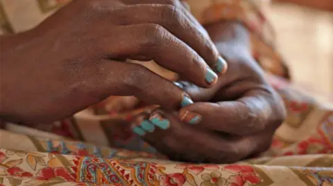 BBC / Hassan Lali Close up of a woman's hands, with blue nail polish.