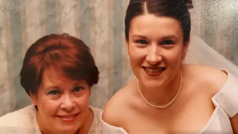 Hayley Bowen Two white women, the one on the left has short, reddish brown hair. The woman on the right has brown hair and is wearing a wedding dress and tiara