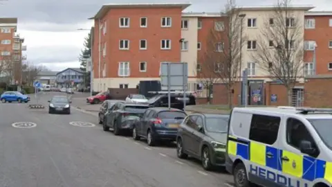 View of Dumballs Road with cars and a police van parked on the right hand side. 