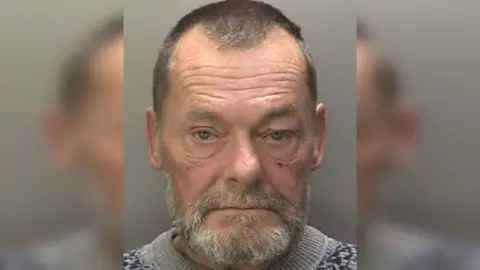 British Transport Police Police custody photograph of Dale Bryan Halliday who has dark hair and a grey beard and is wearing a grey jumper.