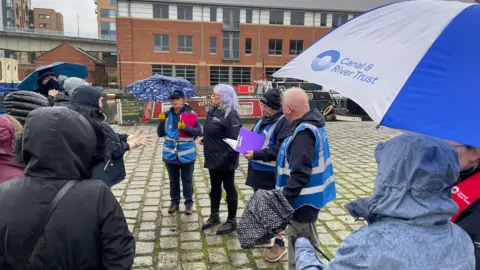 Four volunteers leading a history walk at Victoria Quays surrounded by people with jackets on and hoods up because it's raining