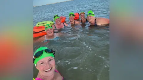 Sheppey Channel Champions Six women in the sea wearing bright green swimming hats and smiling at the camera