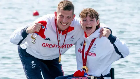 PA Media Great Britain's Lauren Rowles (right) and Gregg Stevenson celebrate with their gold medals , wearing white and red Great Britain training kit in front of the Seine