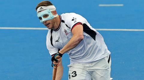 Sam Ward wearing a mask assesses the pitch holding his hockey stick