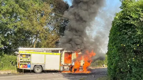 Fire engine caught ablaze on the side of a country road.