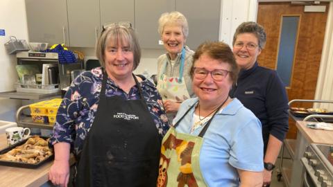 Four volunteers at Waste Not Wednesday pictured in their aprons in the kitchen