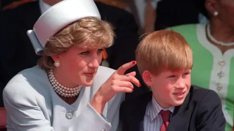 PA Media A young Prince Harry is pictured with his late mother, Diana, Princess of Wales, in 1995. He is wearing a light colored jacket and matching cap. She has short hair and is wearing pearl earrings and a necklace. She is gesturing to show something to Harry who is looking away. He is wearing a dark suit jacket, striped shirt and red tie.